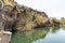 A small lake with fish framed by hexagonal rocks with overgrown bushes and trees on the banks in Yehudia National Natural Park in