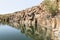 A small lake with fish framed by hexagonal rocks with overgrown bushes and trees on the banks in Yehudia National Natural Park in