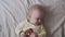 Small light eight-month-old girl playing with a wooden toy lying on the bed in the bedroom, top view, close-up, pastel colors. Bab