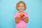 Small little smiling, expressive, positive curly blonde girl holding red juice apple in hands on blue view. Healthy life