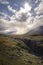 Small lonely hiker standing in enormous cloud and sunlight covered autumn wilderness