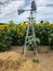 Small metal windmill by field of sunflowers