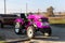 Small mini glamour modern pink new tractor with trailer standing near hangar building farm countryside during sunset or