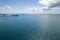 A small motor boat speeds across the water from a coal export port towards shore under a cloudy blue sky with the sun glistening