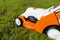 A small motorized electric mower standing on the lawn, it is orange in color.