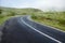 Small narrow asphalt road with bends in a mountains, tourist campervans parked off road in the background. Blue cloudy sky and