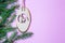 A small nativity scene carved out of wood hangs from a spruce branch in front of a matte pink background. christmas invitation