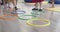 Small nursery school children with female teacher on floor indoors in classroom, doing exercise. Jumping over hula hoop