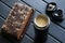 Small office thermos or thermo mug with coffee and milk, piece of chocolate biscuit on dark background made of natural boards. The