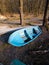 Small old shabby worn wooden rescue boat, painted blue, early spring landscape with bare trees on the bank of a river