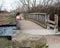 Small old wooded bridge through river with warning sign in spring park and stone in front of