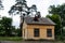 Small one-story house. Yellow building. Brick edifice near the pines. Old house with windows.