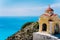 Small orange colored Hellenic shrine Proskinitari on the cliff edge with defocused sea view in the background