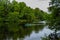 Small passenger rowing boat with family, people floats on pond, lake in park among green trees, bushes, forest in cloudy weather