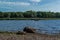 Small passenger rowing boat with people floats on bay of Baltic sea among green trees, bushes, forests in sunny weather. Pebbles s