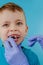 Small patient does not want to open the dentist`s mouth on blue background. Dantist treats teeth. close up view of dentist