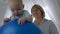 Small patient lies on an inflatable blue ball on the background of professional therapist indoors in backlight