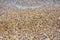 Small pebbles on the shore in a beach with wavy sea. Summer background photo.