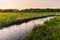 A small picturesque river among a green meadow during sunset. Small river in the countryside.