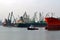 A small pilot ship leads a large red cargo ship at the seaport on a windless autumn day