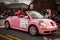 A small pink and decorative car driving in a parade