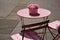 small pink terrace table with flower pot. wood and metal pink foldable patio chairs. outdoor furniture.
