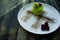 A small pistachio cake with a green coating and decorated with viburnum, confectionery dressing on a black background. Side view