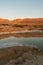 Small pond in a deserted area surrounded by hills under the sunlight and a blue sky