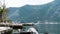 Small port with green mountains and water with moss in the ropes. Ship in kotor bay and coast town. Rock pier for small boats in