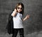 Small positive girl in black and white rock style casual clothing and sunglasses standing and feeling happy with raised hand