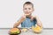 A small preschooler sits at the table and holds French fries in his hands. Fast food, hamburger, French fries, and gravy are on