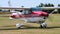 Small private light aircraft in red and white livery taxiing on a grass airfield