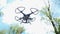 Small quadcopter drone stay in air, four little propellers quickly spin, sky and trees on background. Popular mobile device with e