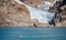 Small red boat crossing in front of massive front of a glacier in Prince Christian Sound, South Greenland