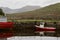 A small red boat is docked along a quiet lake in rural Connemara in western Ireland