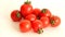 Small red Cheri tomatoes with green tails lie scattered on a white background close up