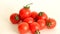 Small red Cheri tomatoes with green tails lie scattered on a white background close up