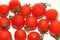Small red Cheri tomatoes with green tails lie scattered on a white backgroundred tomatoes with green tails in a glass vase on a wh