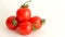 Small red Cherry tomatoes with green tails lie scattered on a white background close uy