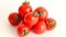 Small red Chery tomatoes with green tails lie scattered on a white background close uy