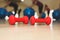 Small red dumbbells on the wooden floor. Fitness gears in the gym with girls doing exercises with balls on the background. Sport