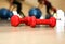 Small red dumbbells on the wooden floor. Fitness gears in the gym with girls doing exercises with balls on the background. Sport