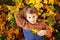 A small red haired boy in a sweater looks at the camera and smiles lying in the fallen yellow leaves of an autumn Park