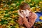 A small red haired boy in a sweater looks at the camera and smiles lying in the fallen yellow leaves of an autumn Park