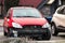 A small red hatchback car with missing frontal par after a traffic accident with radiator visible