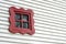 A small red painted old shabby window on a white wall