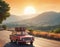 A small red retro car drives off into the distance towards the hills above which there is a huge orange sun, tourist suitcases on