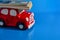 A small red toy car carries on the roof a stack of paper banknotes, blue background. The concept of costs for maintenance, car