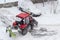 Small red tractor with snow plow in courtyard during snowfall