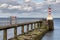 A small red and white lighthouse on the end of a jetty